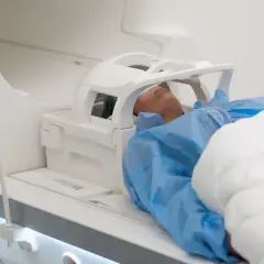 Pacjent leży w aparacie do rezonansu głowy, otoczony białym sprzętem medycznym.
