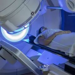 Kobieta leży na stole zabiegowym podczas radioterapii. Zielone linie lasera wyznaczają pole napromieniania.