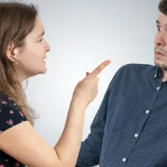 Kobieta z wyrzutem wskazuje palcem na mężczyznę, który wygląda na zaskoczonego. Scena przypomina dramat z motywem zazdrości, jak w "Zespole Otella".