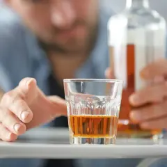 Mężczyzna sięga po szklankę z alkoholem, grozi mu zatrucie alkoholowe.