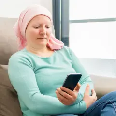 Kobieta w chustce na głowie, po chemioterapii, sprawdza telefon. Może szuka informacji o 500 plus dla chorych na raka ZUS.