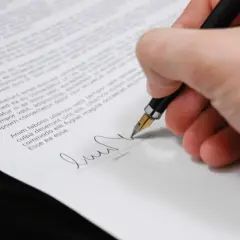 Dłoń z piórem podpisuje dokument, być może oświadczenie o odrzucenie spadku.