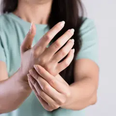 Kobieta trzyma się za nadgarstek, odczuwając drżenie rąk.