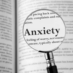 Lupa powiększa hasło "Anxiety" w książce, opisując uczucie niepokoju, które może towarzyszyć fobiom.