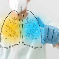Dłoń w niebieskiej rękawiczce dotyka schematu płuc, ukazując rozstrzenie oskrzeli.