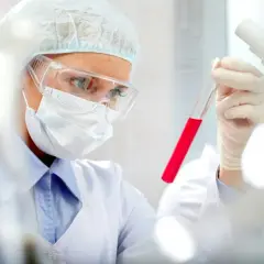 Naukowczyni w okularach i masce analizuje próbówkę z czerwonym płynem, badając poziom prokalcytoniny.