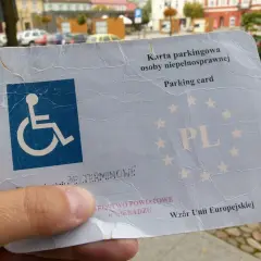 Karta parkingowa dla niepełnosprawnych, z symbolem wózka inwalidzkiego i oznaczeniem PL. Dokument uprawniający do parkowania.