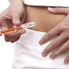 Osoba wykonuje zastrzyk podskórny z leku Clexane. Dłoń trzyma strzykawkę, a druga ręka przytrzymuje skórę brzucha.