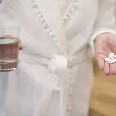 Dłoń trzyma garść białych tabletek i szklankę wody. Pytanie brzmi: kiedy brać magnez?