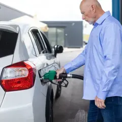 Starszy mężczyzna tankuje biały samochód. Może to być związane z ulgą rehabilitacyjną na samochód, ułatwiającą codzienne funkcjonowanie.