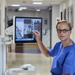 Lekarz w niebieskiej koszuli wskazuje na ekranie komputerowym obraz z planem biopsji prostaty.
