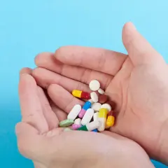 Dłonie trzymają garść kolorowych tabletek i kapsułek, wśród nich leki psychotropowe.