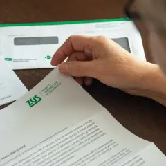 Dłoń przegląda dokumenty ZUS dotyczące zasiłku chorobowego i innych świadczeń.