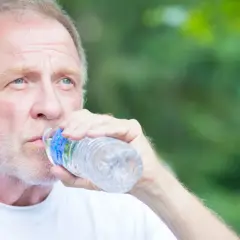 Starszy mężczyzna z ręcznikiem na ramieniu pije wodę z butelki. Może to być sposób na zapobieganie odwodnienie objawy.