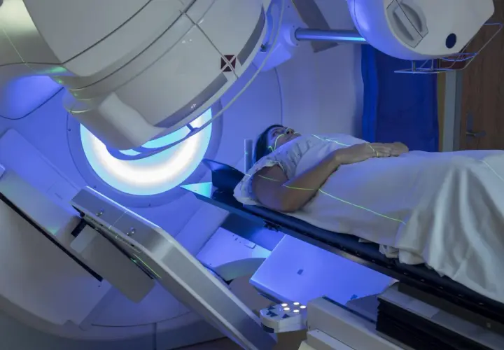 Kobieta leży na stole zabiegowym podczas radioterapii. Zielone linie lasera wyznaczają pole napromieniania.