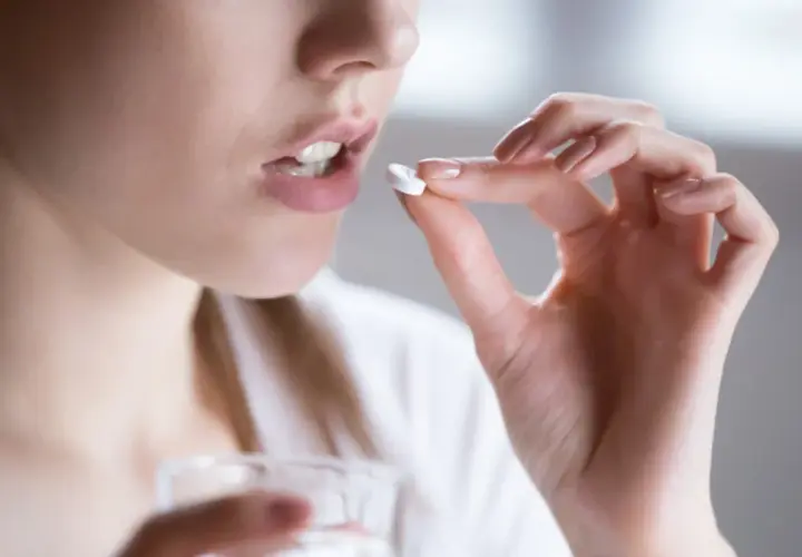 Kobieta bierze tabletkę clindamycin mip 600, trzymając ją palcami i szklankę wody.