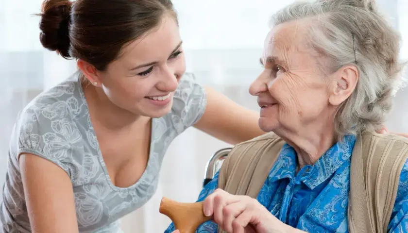 Młoda kobieta wspiera starszą panią, która trzyma laskę. To może być czas urlopu opiekuńczego 5 dni, pełen troski i bliskości.
