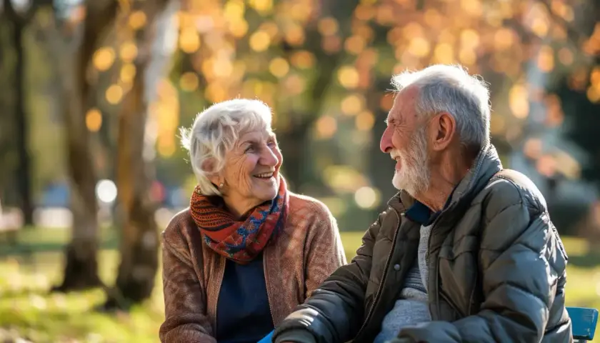 Uśmiechnięta para seniorów cieszy się jesiennym dniem w parku. Dobre samopoczucie zawdzięczają pewnie zdrowej diecie i codziennej multiwitaminie.
