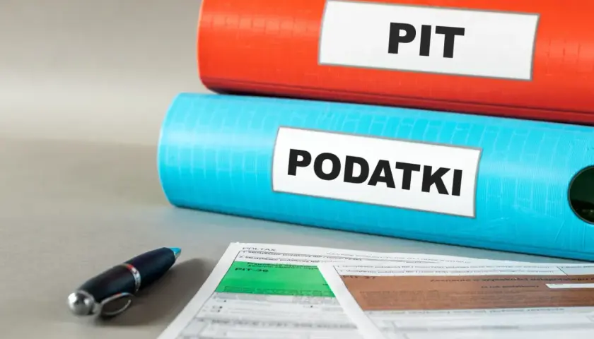 Dwa segregatory z napisami "PIT" i "PODATKI" oraz formularze podatkowe i długopis. Czas na ulgę podatkową!