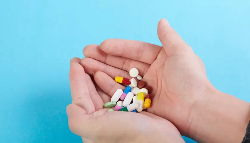 Dłonie trzymają garść kolorowych tabletek i kapsułek, wśród nich leki psychotropowe.