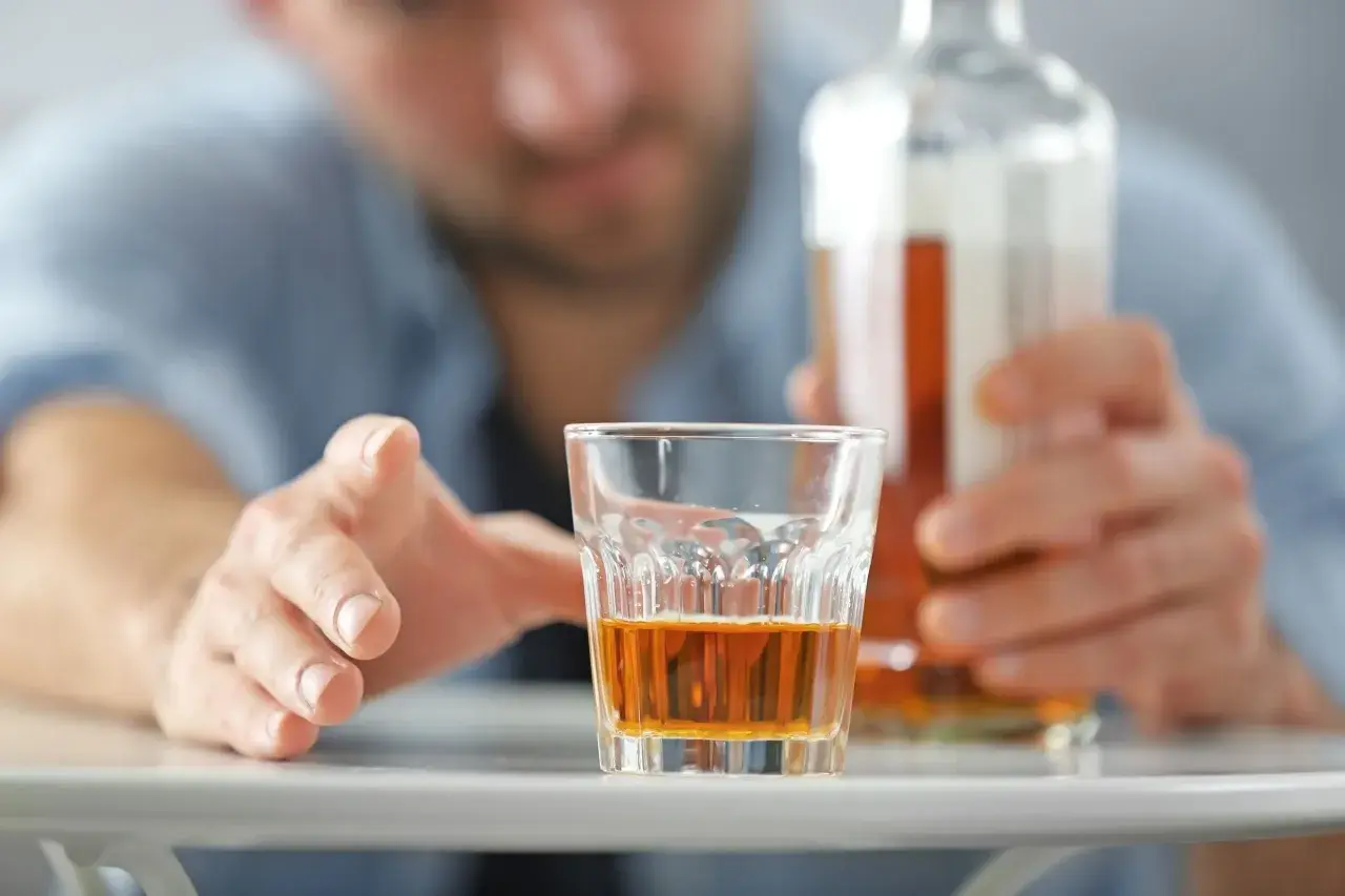 Mężczyzna sięga po szklankę z alkoholem, grozi mu zatrucie alkoholowe.