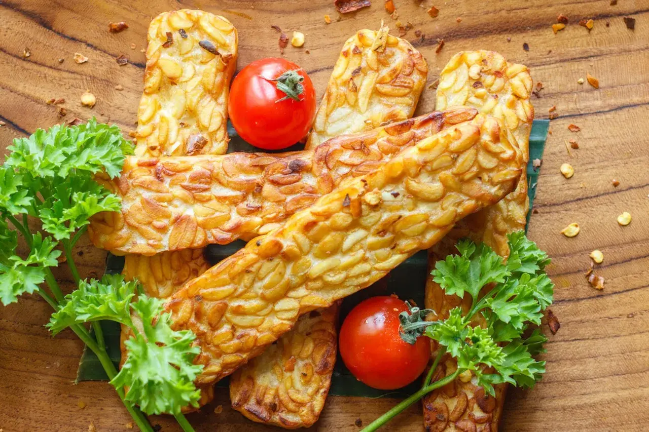 Złociste kawałki tempeh, smażone na złoto, z pomidorkami i natką pietruszki. Tempeh co to? To pyszna, roślinna alternatywa!