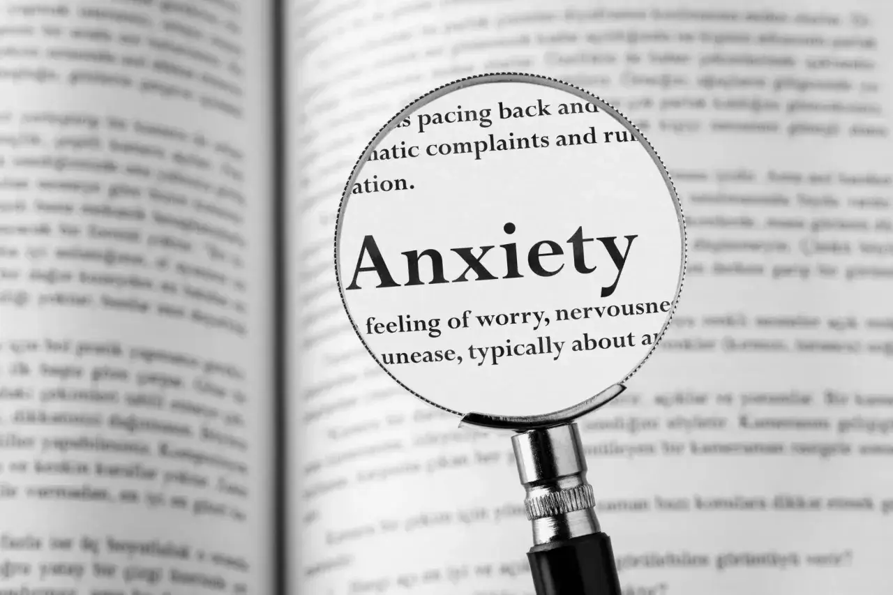 Lupa powiększa hasło "Anxiety" w książce, opisując uczucie niepokoju, które może towarzyszyć fobiom.
