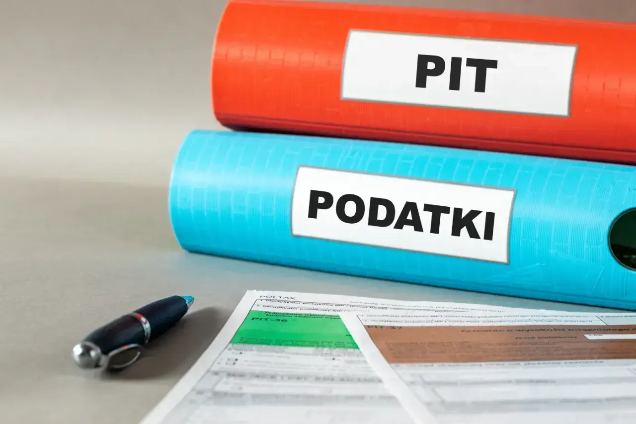 Dwa segregatory z napisami "PIT" i "PODATKI" oraz formularze podatkowe i długopis. Czas na ulgę podatkową!