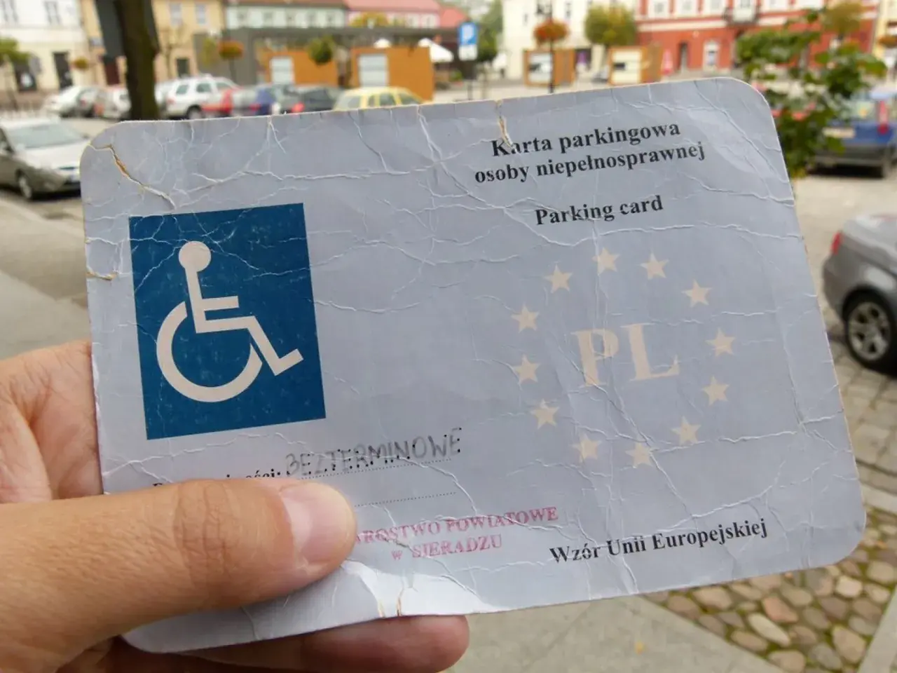 Karta parkingowa dla niepełnosprawnych, z symbolem wózka inwalidzkiego i oznaczeniem PL. Dokument uprawniający do parkowania.