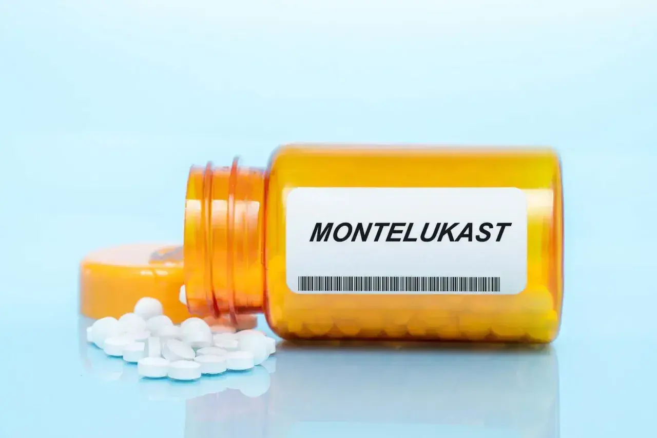 Pomarańczowa buteleczka leku z etykietą "MONTELUKAST" i rozsypanymi tabletkami.