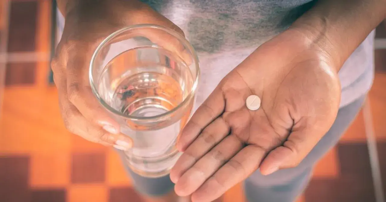 Dłoń trzyma szklankę wody i tabletkę, być może Efferalgan Codeine, by złagodzić ból.