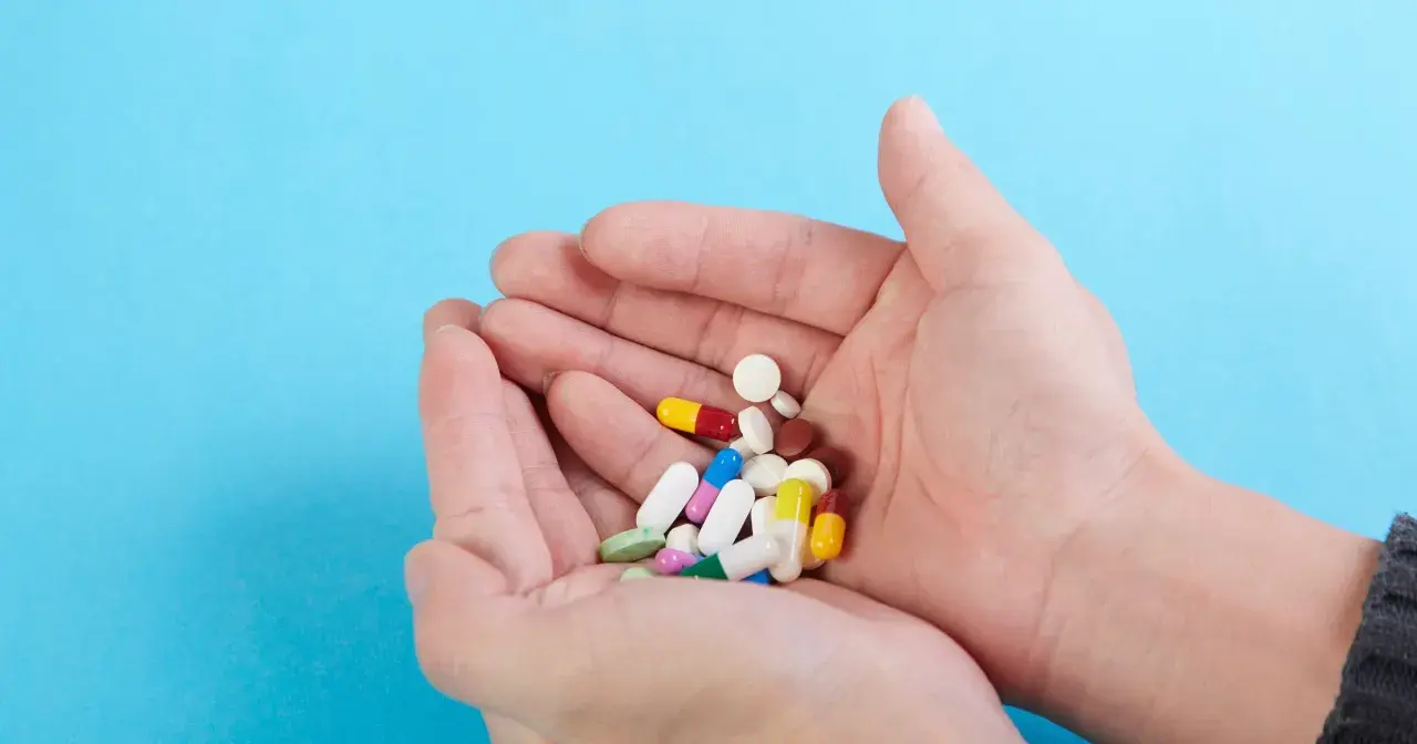 Dłonie trzymają garść kolorowych tabletek i kapsułek, wśród nich leki psychotropowe.