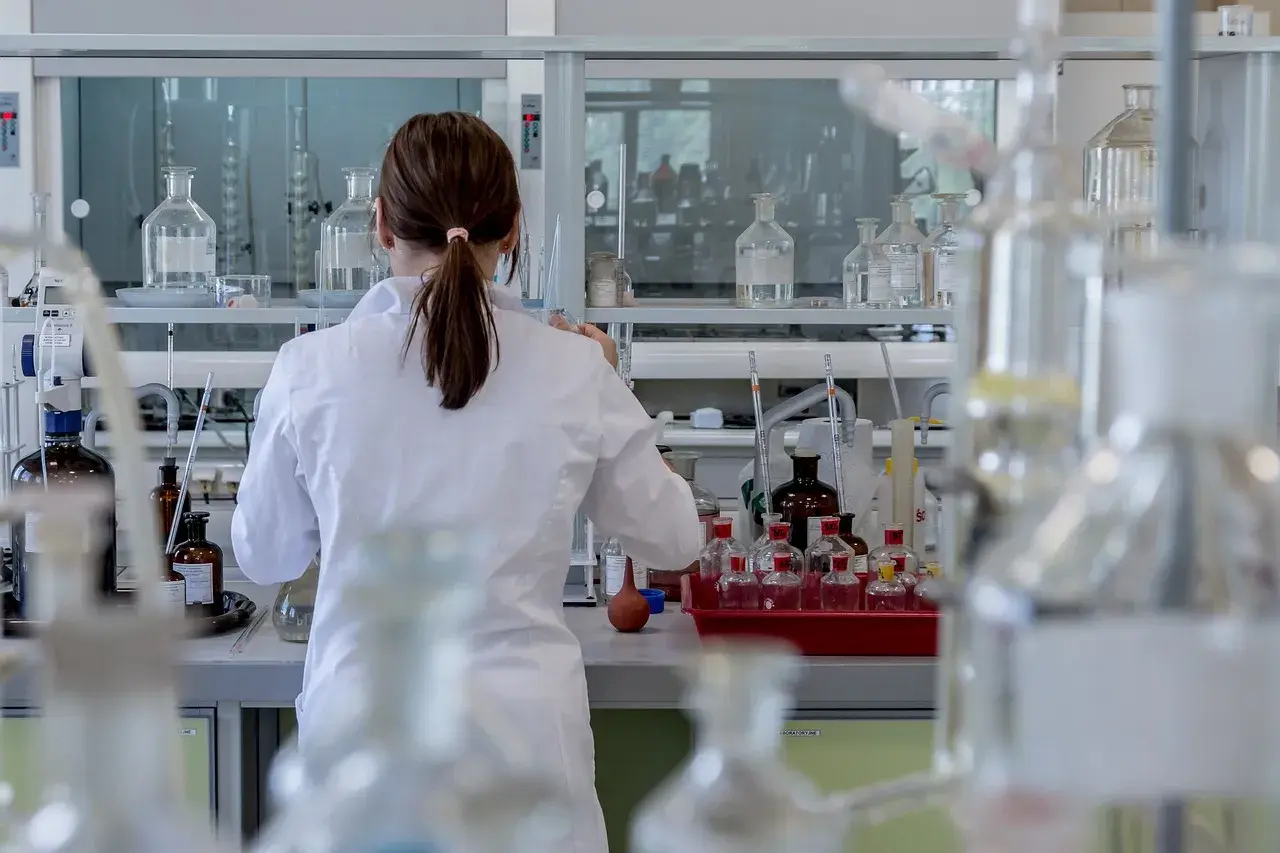 Naukowczyni w białym fartuchu pracuje w laboratorium, otoczona szkłem laboratoryjnym. Analizuje próbki, być może badając rdw-cv.