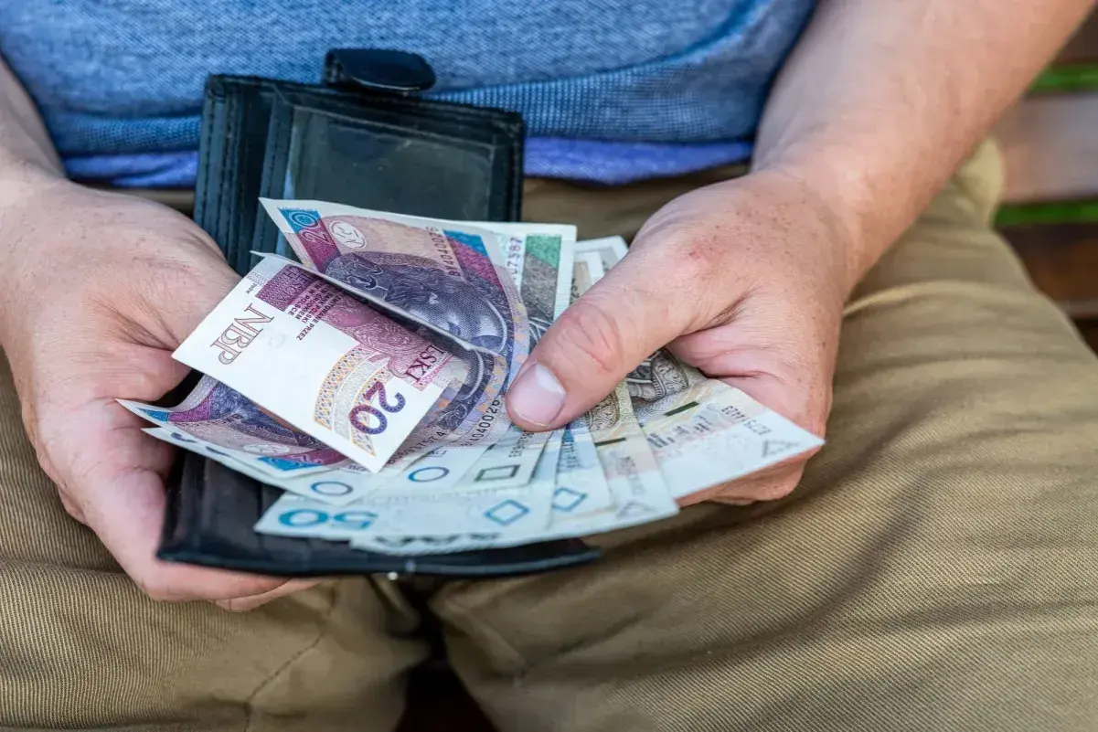 Dłonie trzymają portfel z polskimi banknotami. Czy to dodatek pielęgnacyjny, czy zasiłek pielęgnacyjny?
