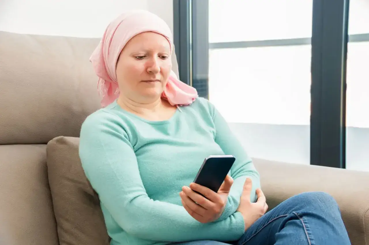 Kobieta w chuście na głowie przegląda telefon, być może szukając informacji o 500 plus dla chorych na raka ZUS.