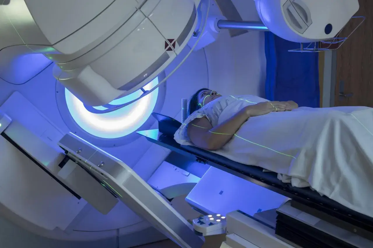 Kobieta leży na stole zabiegowym podczas radioterapii. Zielone linie lasera wyznaczają pole napromieniania.