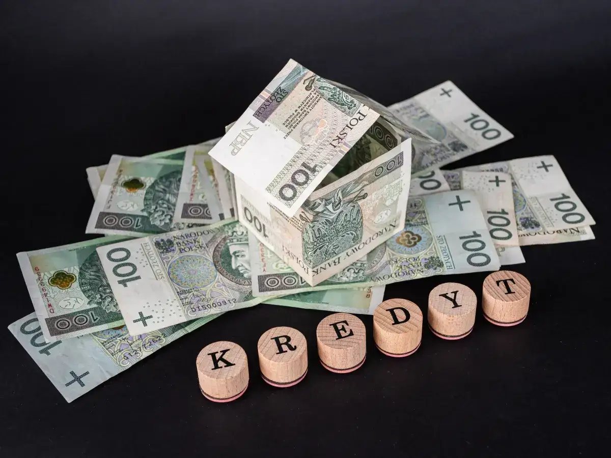 Dom z banknotów 100 zł, litery KREDYT. Symbolizuje sankcję kredytu darmowego.