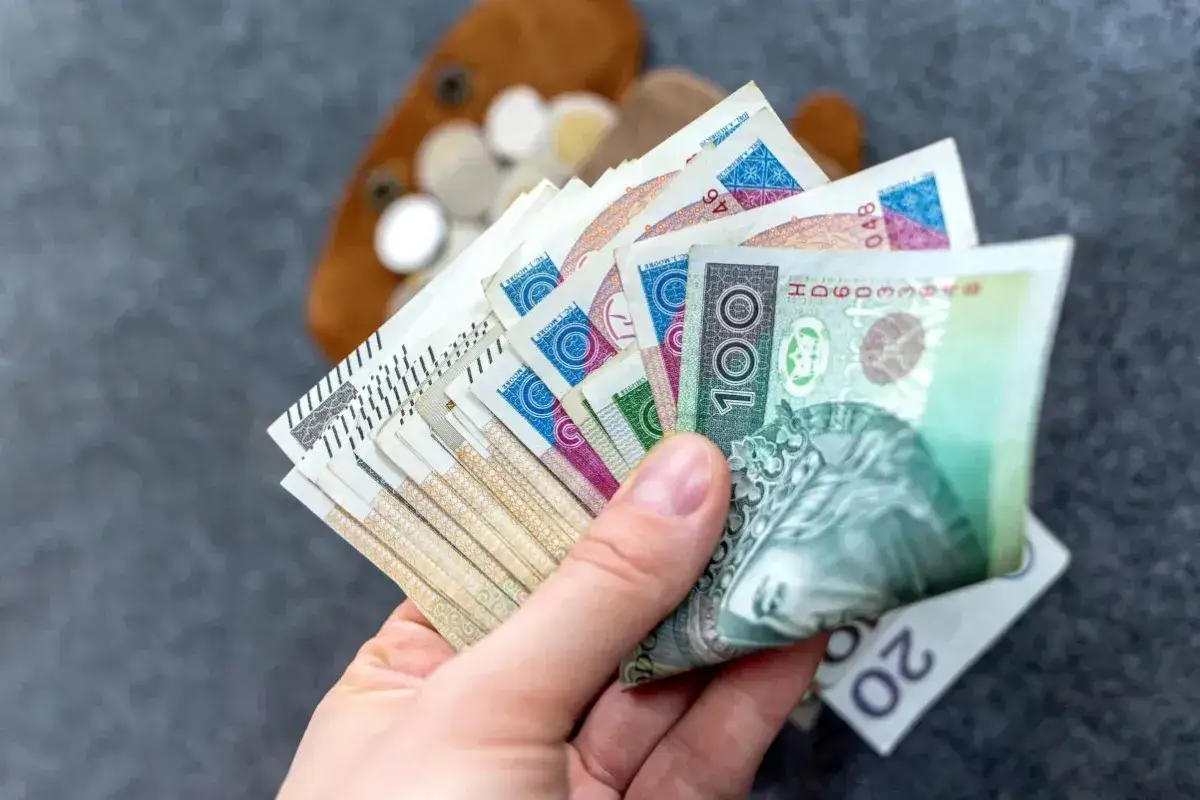 Dłoń trzyma polskie banknoty, symbolizujące dodatek pielęgnacyjny i zasiłek pielęgnacyjny.