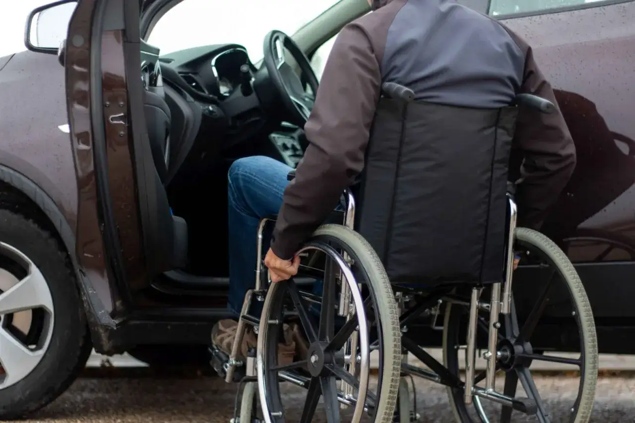 Mężczyzna na wózku inwalidzkim wsiada do samochodu. Ułatwienie dostępu do pojazdu to ważny element ulgi rehabilitacyjnej na samochód.